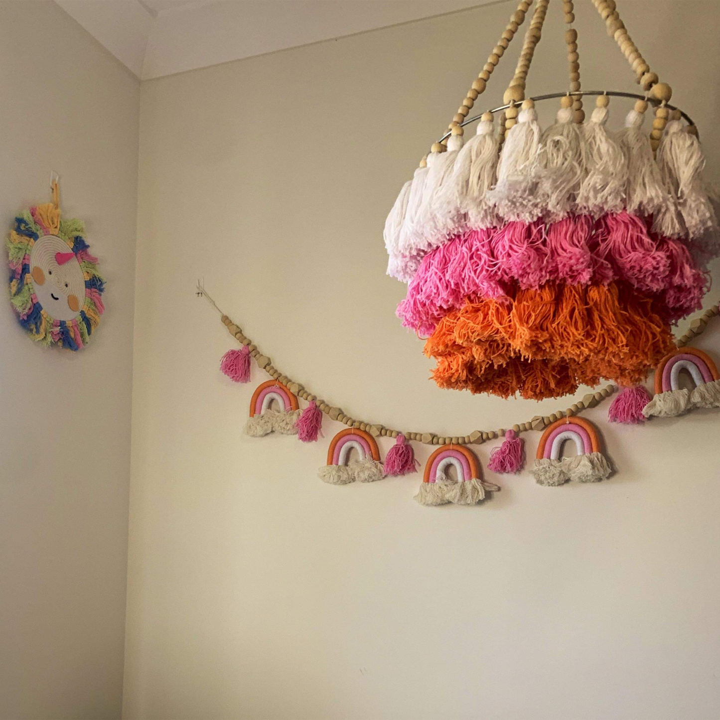 A hanging tassel mobile with beaded tassels in pink, orange, and white, with a wooden ring at the top for hanging.