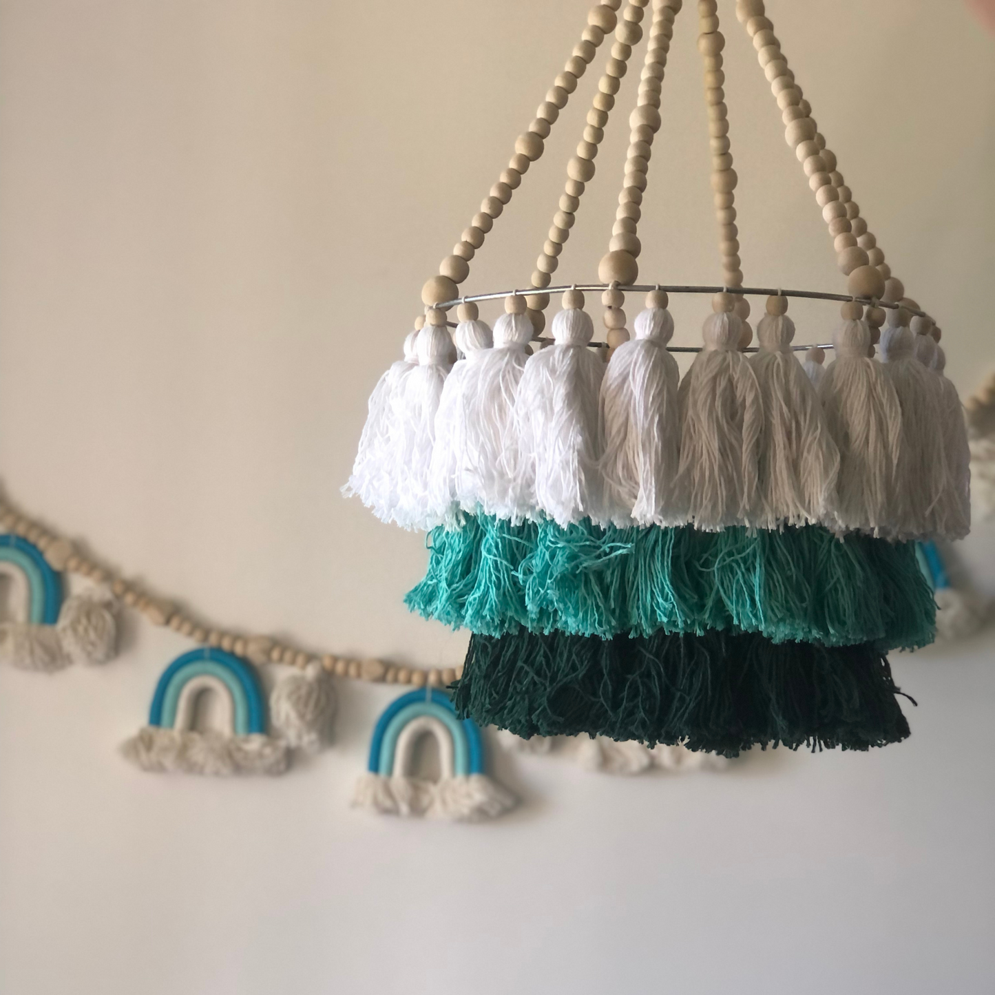 A hanging tassel mobile with beaded tassels in green, dark green and white, with a wooden ring at the top for hanging.