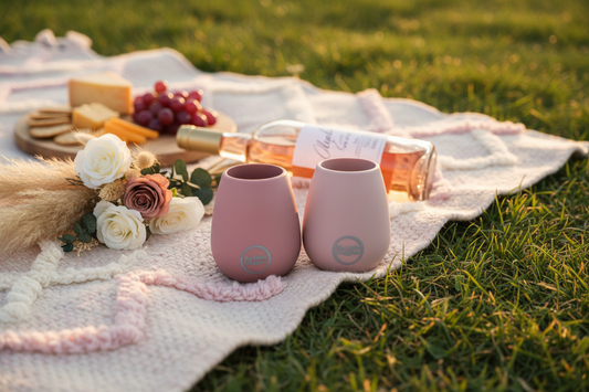 Two pink silicone stemless wine tumblers on a boho picnic rug with rosé wine, roses and a cheese board — a perfect Mother's Day gift from My Baby and Me