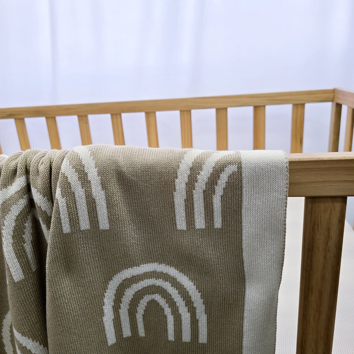 Australian made knitted rainbow blanket draped over side of wooden cot