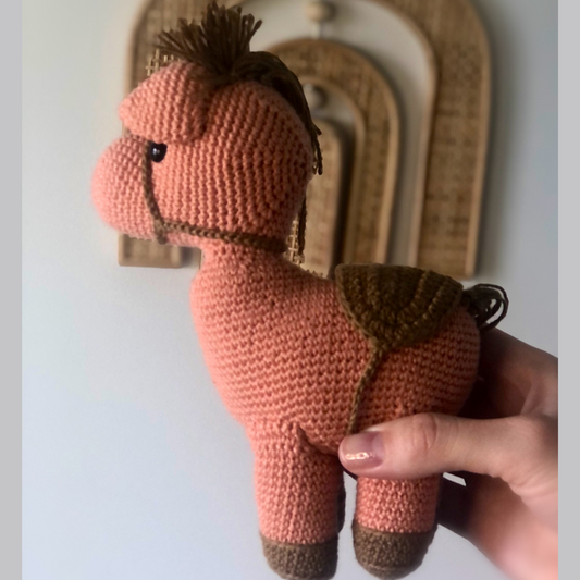 Crocheted doll shaped like a pony with a brown saddle and mane.