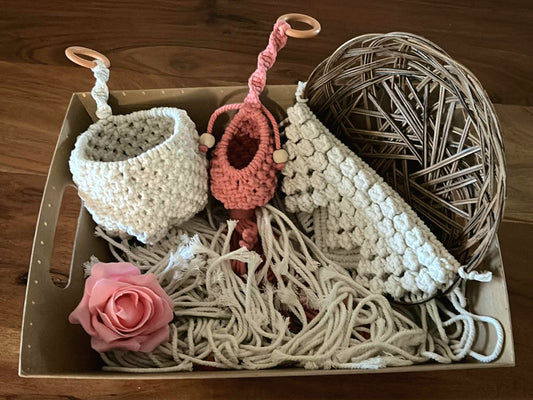 A collection of macrame woven basket, a  small airplant pods in various colours,  and a large natural beige pot holder arranged neatly in a box