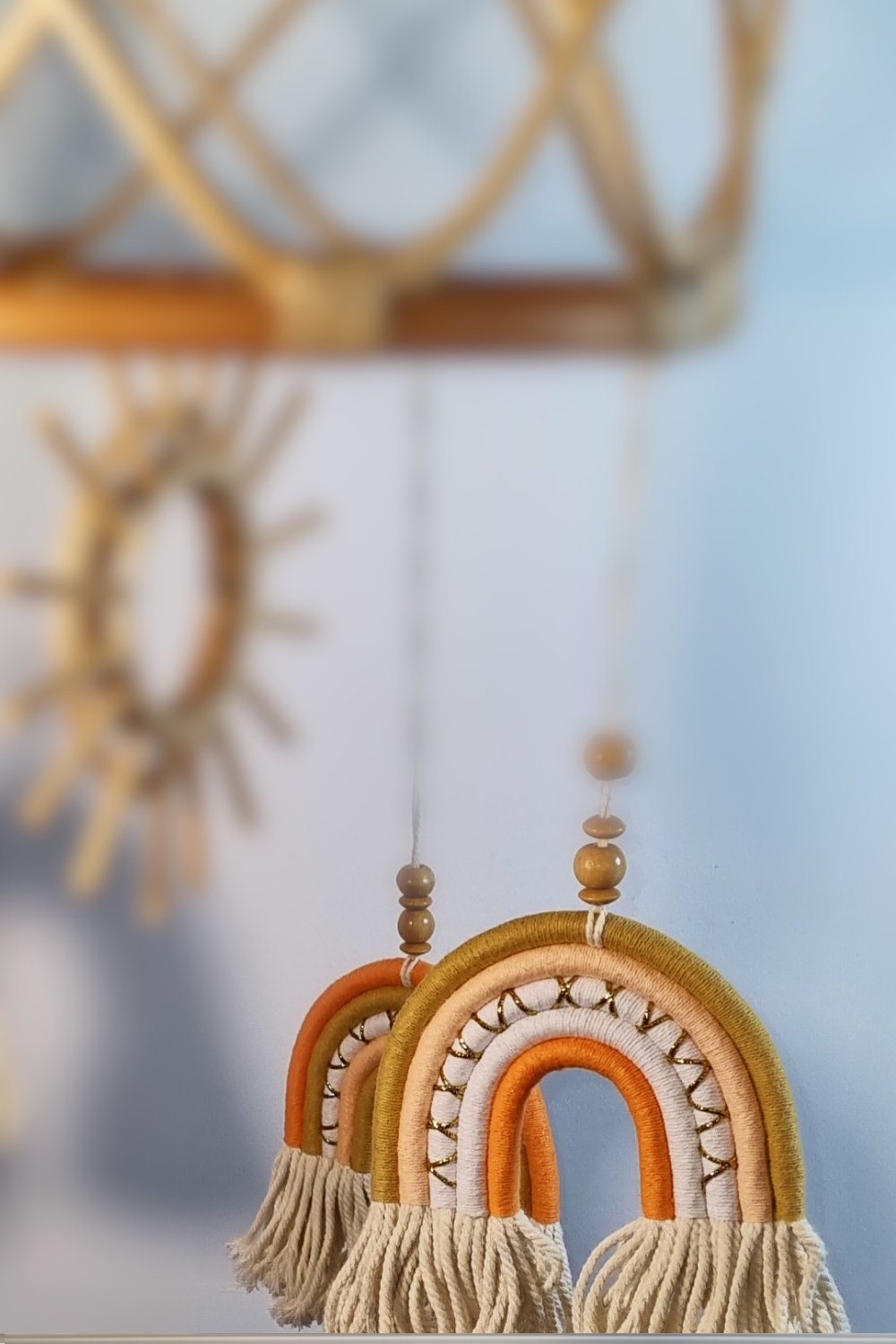 Close-up of orange and gold macrame rainbow detail on boho rattan sun baby mobile with wooden sun centrepiece in background