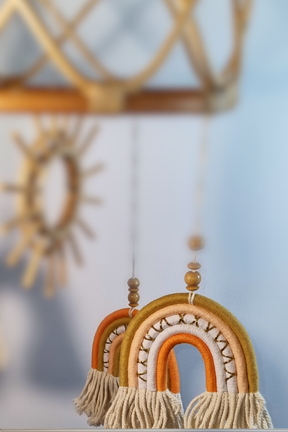 Close-up of orange and gold macrame rainbow detail on boho rattan sun baby mobile with wooden sun centrepiece in background