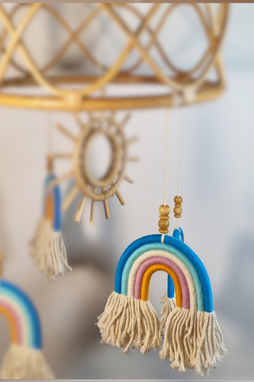 Close-up of orange and gold macrame rainbow detail on boho rattan sun baby mobile with wooden sun centrepiece in background