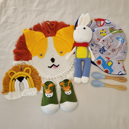 Darcy baby gift box flat lay showing fox wall hanging, lion keyring, giraffe baby shoes, crochet bunny doll, bucket hat and Kubbi Co spoons - baby gift Australia