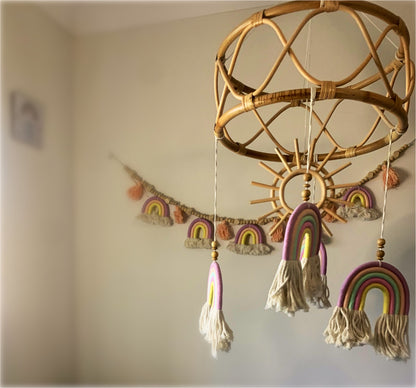 A handcrafted exclusive rattan mobile with a wooden sun and bamboo frame design, adorned with macrame rainbow decorations in a nursery setting.